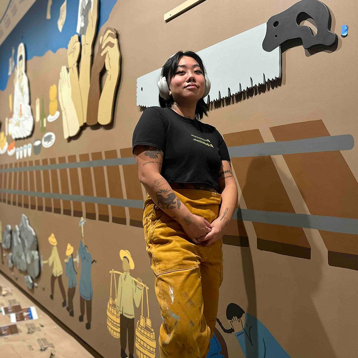 Monyee洲 standing in front of a wall full of cultural art